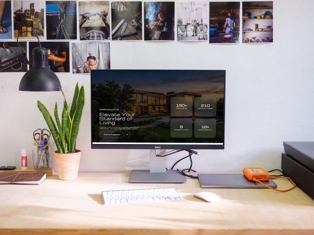 A silver MacBook Air 15-inch laptop resting on a jagged, dark gray rock surface, displaying a luxury real estate website against a soft gray background.